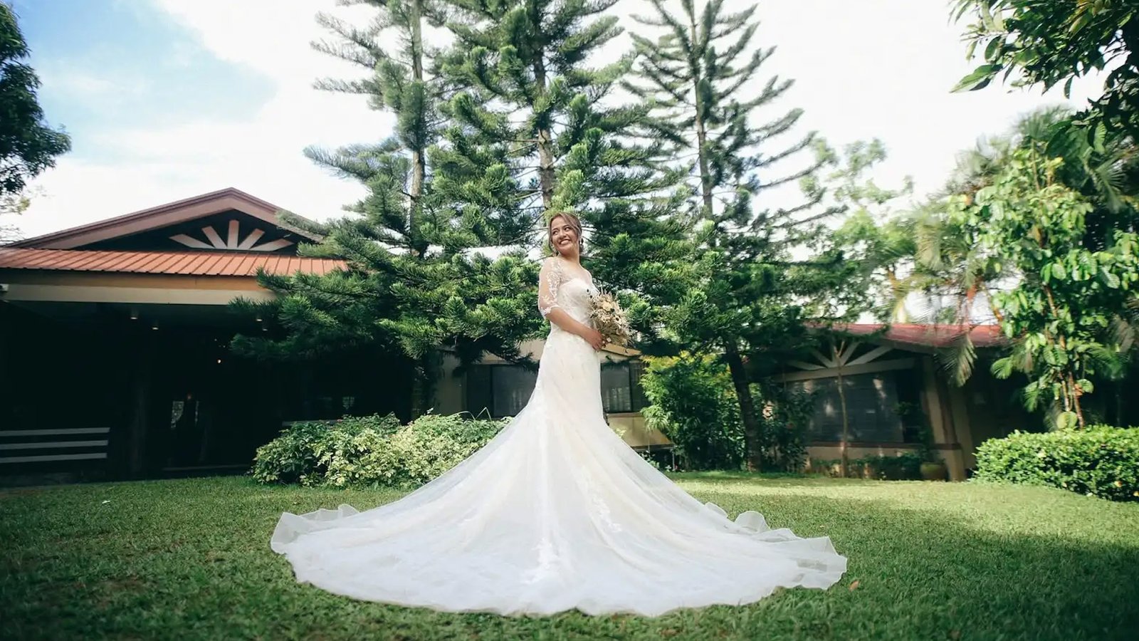 Bride in a flowing gown stands on the garden lawn at Savanna Farm Tagaytay, framed by tall pine trees under daytime light